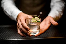 A bartender holds out a gin and tonic garnished with cucumber