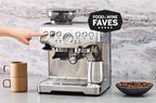 Hand pressing a button on the Breville Barista Express displayed with cups and a bowl with coffee on a grey counter