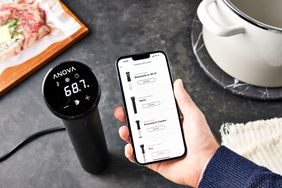 Hand holding a phone next to the Anova Culinary Precision Cooker Nano