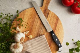 A breadknife laying on a round cutting board next to a dishtowel and garlic