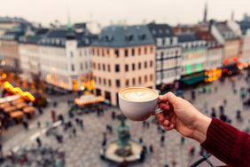 A hand holding a latte over a square in Copenhagen