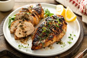 Chicken breasts with fresh herbs, whole and sliced on a white plate