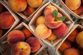 Several quarts of ripe peaches with one showing off its leaves