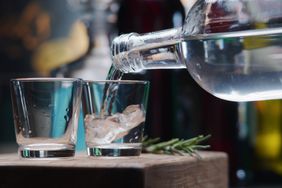 Two shots of clear liquor being poured into shot glasses. 