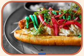 A hot dog topped with pickled onion and herbs